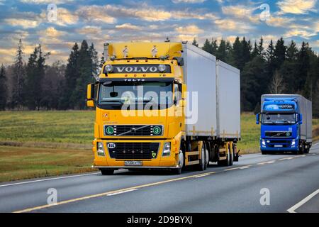 Yellow, customised Volvo FH freight transport truck followed by blue Volvo FH at speed on highway 2. Jokioinen, Finland. October 30, 2020. Stock Photo