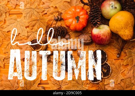 top view of autumnal decoration and food scattered from wicker basket near hello autumn lettering on golden foliage Stock Photo