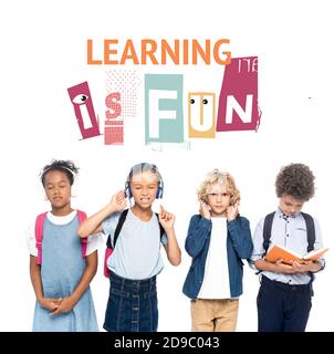 multicultural schoolkids listening music in wireless headphones near curly boy reading book and learning is fun lettering on white Stock Photo