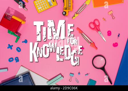 top view of stationery and toy school bus near time for knowledge lettering on pink Stock Photo