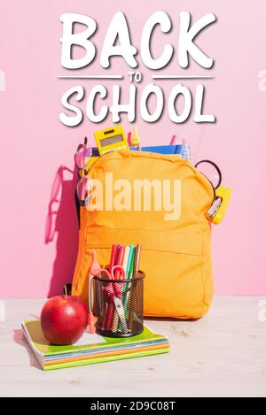 packed school backpack near notebooks, pen holder with felt pens and scissors, ripe apple and beck to school lettering on pink Stock Photo