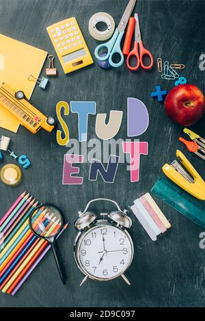 top view of frame with apple, toy school bus, vintage alarm clock and school supplies on black chalkboard with student lettering Stock Photo