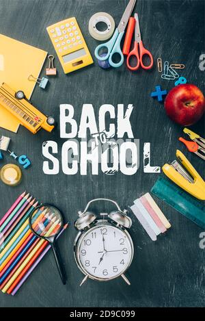 top view of frame with apple, toy school bus, vintage alarm clock and school supplies on black chalkboard with back to school lettering Stock Photo