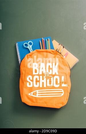 top view of backpack packed with school stationery on green chalkboard with back to school lettering and pencil illustration Stock Photo