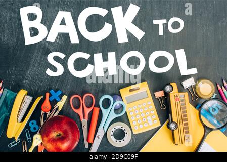top view of ripe apple, calculator and school supplies on black chalkboard with back to school lettering Stock Photo