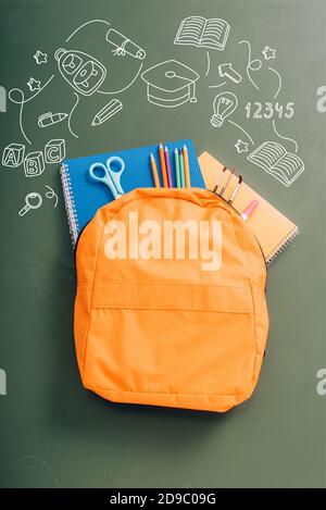 top view of backpack packed with school stationery on green chalkboard with illustration Stock Photo