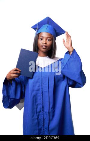 African-American beautiful woman in a blue robe and hat, on a white isolated background holding a diploma of higher education in her hands Stock Photo