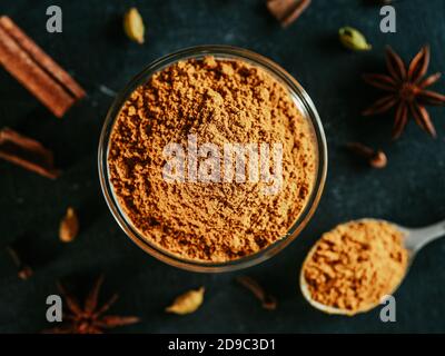 Indian or pakistani masala powder in spoon and small glass bowl. Close up view of homemade dry curry garam masala mix spices blend on dark background. Stock Photo