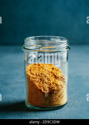 Indian or pakistani masala powder in glass jar. Homemade dry curry garam masala mix spices blend on dark gray background. Vertical Stock Photo