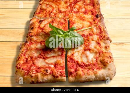 Tasty square cut pizza with a nice green sprig of basil leaves on wooden surface Stock Photo
