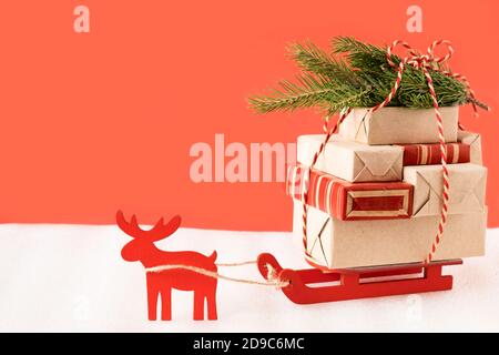 Toy reindeer and sleigh delivering christmas gifts and tree on festive red background. Stock Photo
