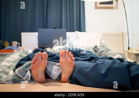 man in bed with laptop focus on feet Stock Photo