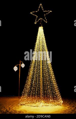 Bright shiny christmas tree made from string lights on sandy beach Stock Photo