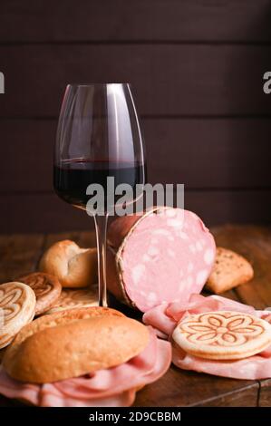 A glass of red wine, mortadela, Tigelle and different breads on a wooden table. A traditional pre-dinner starter in the northern Italian region of Emilia Romagna. Copy space. Vertical photo. Stock Photo