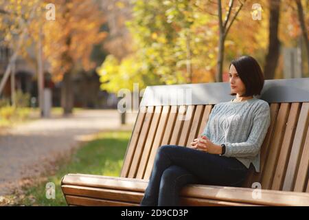 Young beautiful woman sitting on bench in autumn park. Stock Photo