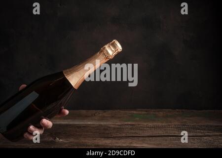 A bottle of champagne without a label in the hand of a woman on a wooden background. Stock Photo