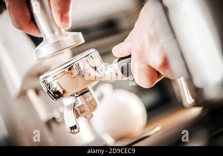 Caucasian Barista Preparing Espresso. Portafilter Coffee Compacting by Metal Tamper Close Up. Stock Photo