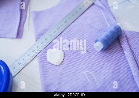 Top view: professional equipment and tools for sewing: pins, thread spools, piece of cloth, chalk, ruler on table at atelier. Fashion, needlework Stock Photo