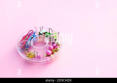 Colorful pins and paper clips in plastic round storage on pink soft background Stock Photo