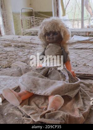 An old doll with a dirty face on a bed in an abandoned kindergarten. Radiation-contaminated room in Chernobyl. Stock Photo