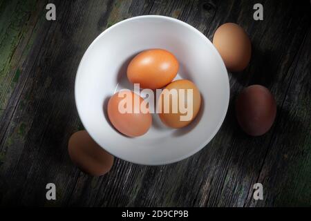 Close up Photo of Three Fresh Eggs In White Ceramic Bowl and Three Others on Wooden Decayed Background Stock Photo