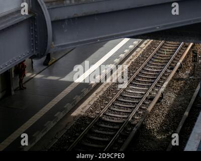 a train platform viewed from a bridge with a single figure standing just out of the light Stock Photo