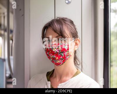 young woman wearing a red floral face mask whilst travelling on a train Stock Photo