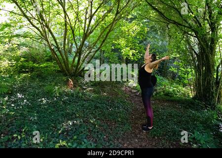 Side view of happy young woman with raised arms standing in forest Stock Photo