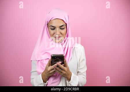 Young beautiful arab woman wearing islamic hijab over isolated pink background texting with her phone Stock Photo