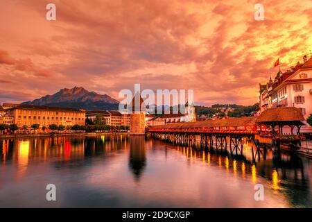 Mount Pilatus mountain overlooking the skyline of Lucerne town of Switzerland. Dusk cityscape with city lights and Chapel Bridge with Water Tower on