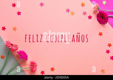 Feliz Cumpleanos means Happy Birthday in Spanish language. Flat lay, gerbera flowers on pink paper Stock Photo