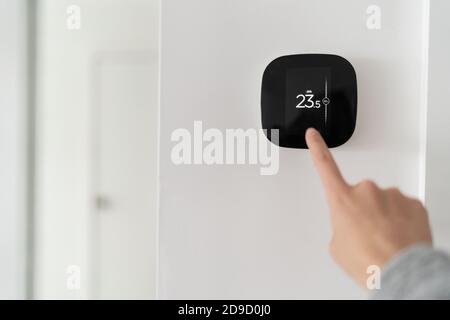 Smart home digital thermostat touch screen woman touching touchscreen to adjust temperature of heating in living room wall Stock Photo