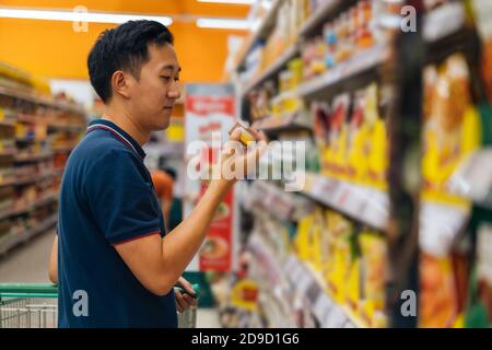 Side view of Asian man shopping in grocery store, buying food, standing in supermarket aisle looking at products, grocery shopping Stock Photo