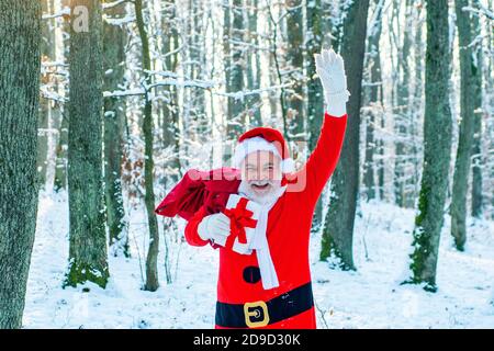 New year concept. Delivery christmas gifts. Santa Claus comes with gifts from the outside. Santa Claus going with a bag of gifts in the winter on snow Stock Photo