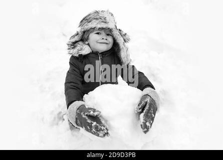 Snowman and funny child the friend is standing in winter hat and scarf with red nose. Joyful kid Having Fun with snowman in Winter Park. Winter Stock Photo