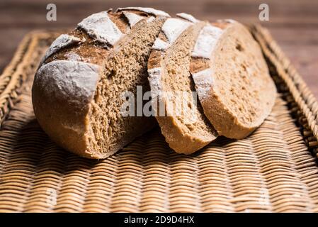 Loaf of brown bread with two slices cut on a brown wicker tray Stock Photo