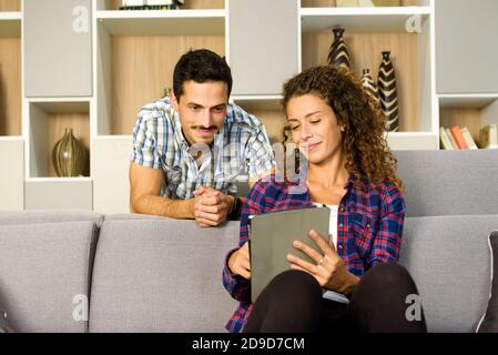 Young couple streaming media on a tablet-pc sitting together watching it in their living room with pleased smiles in a personal entertainment concept Stock Photo