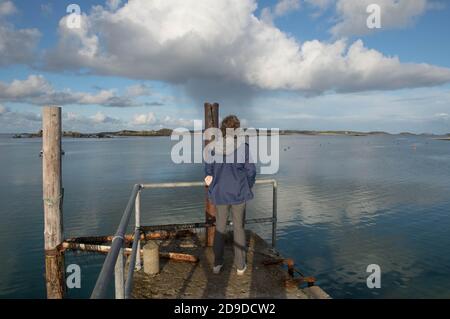 Female Standing at the End of a Concrete Quay Admiring the Calm Sea Water of Grimsby Sound on the Island of Tresco in the Isles of Scilly England, UK Stock Photo