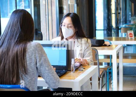 Two female students wearing face masks working on their computers in a restaurant. New normal in restaurants. Coronavirus pandemic.