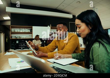 Two young entrepreneurs researching on laptop and digital tablet during lunch break in office foyer  Stock Photo