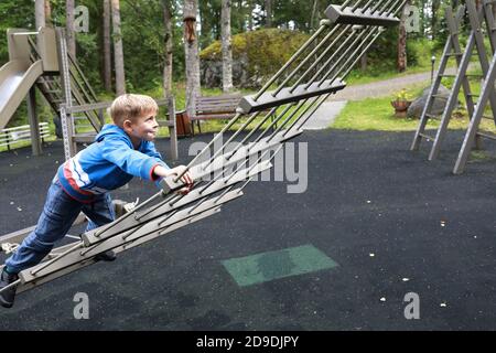 Child crawling on hanging ladder at outdoor playground Stock Photo