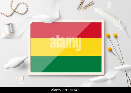 Bolivia flag in wooden frame on white creative background. White theme, feather, daisy, button, ribbon objects. Stock Photo