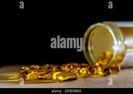 Close-Up of yellow pills of Gold fish oil for good health on wooden table and black background. Food dietary supplement, salmon fish oil softgel Omega pharmaceutical medicine vitamin D oil capsules.