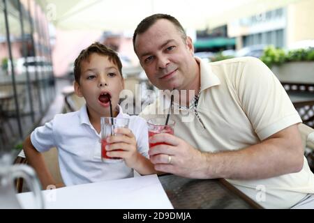 Father and his son drinking juice on terrace of restaurant Stock Photo