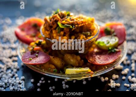 Close up shot of spicy tasty sabudana khichdi or sago ball khichdi along with some sliced tomatoes, some cut lemons in a glass plate, and raw sago bal Stock Photo