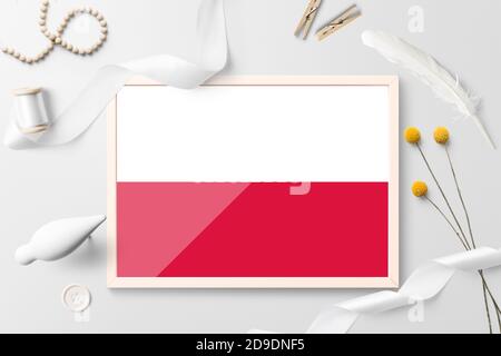 Poland flag in wooden frame on white creative background. White theme, feather, daisy, button, ribbon objects. Stock Photo