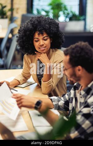 Two young diverse coworkers analyzing sales report while working together in the office. Business and teamwork concept Stock Photo