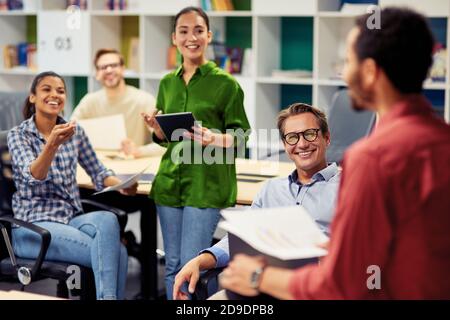 Positive team. Group of young happy multi racial business people communicating and sharing ideas while working together in the modern office. Teamwork and cooperation concept Stock Photo