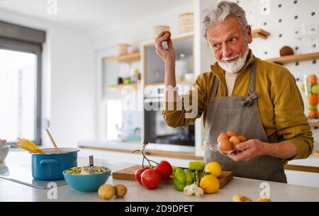 Happy retired senior man cooking in kitchen. Retirement, hobby people concept Stock Photo