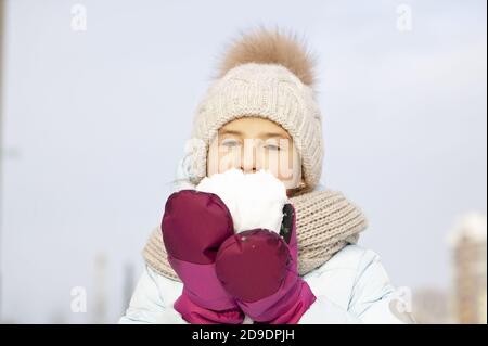Winter portrait of a beautiful girl in a winter knitted hat. Girl holding snow. Stock Photo
